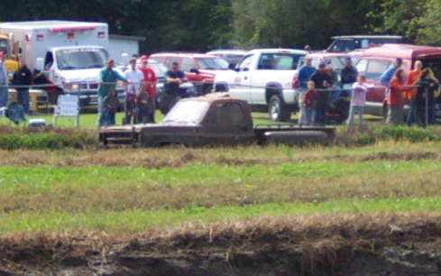 Brown pickup truck partially submerged in muddy grass, side view