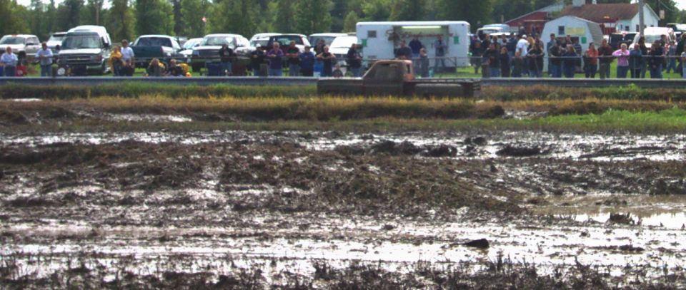 Truck driving through a mud bog with spectators in the background
