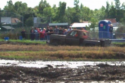 1979 Ford Bronco - A crowd watches as a pickup truck navigates through a muddy obstacle course.