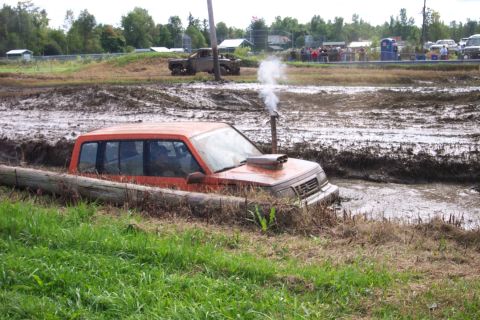 1979 Ford Bronco - An orange SUV is stuck in a mud pit with smoke coming from its exhaust pipe.