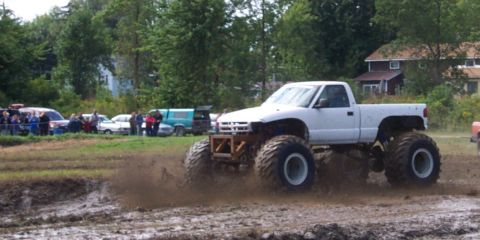 1979 Ford Bronco - A white monster truck with oversized tires churns through a muddy track during an event.