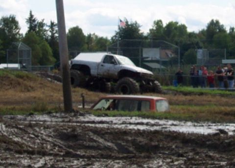 1979 Ford Bronco - A modified pickup truck navigates a muddy incline while a red SUV is stuck in the mud below.