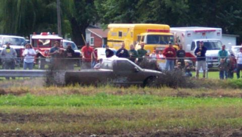 1979 Ford Bronco - A pickup truck is stuck in the mud during an event, with onlookers and emergency vehicles present.