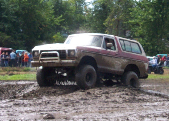 Mud-covered 1978 Ford Bronco with lifted suspension driving through mud