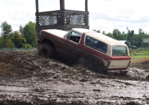 1979 Ford Bronco - A red and white Ford Bronco navigates a muddy obstacle course.