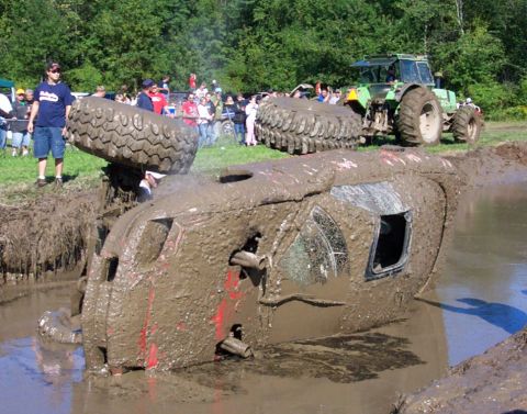 1979 Ford Bronco - A vehicle is stuck in a mud pit during an event, with a tractor and onlookers present.