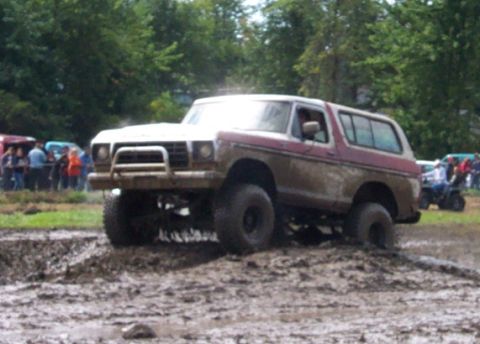 1979 Ford Bronco - This lifted SUV is navigating a challenging mud course, with spectators gathered to watch the event.
