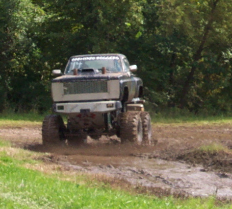 1979 Ford Bronco - A lifted truck with oversized tires navigates a muddy track, kicking up water and dirt.