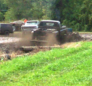 1979 Ford Bronco - Multiple trucks are engaged in a mud bogging event, kicking up dirt and water.