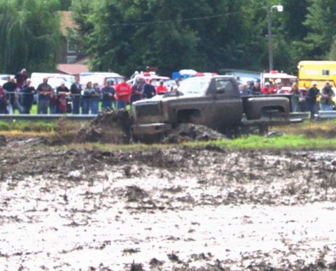 1979 Ford Bronco - A truck is stuck in a mud pit during an event, with a crowd of people watching from the side.