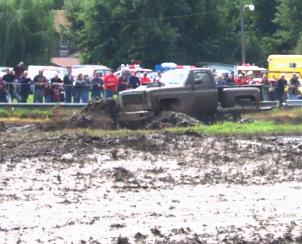 Truck stuck in mud pit with spectators watching