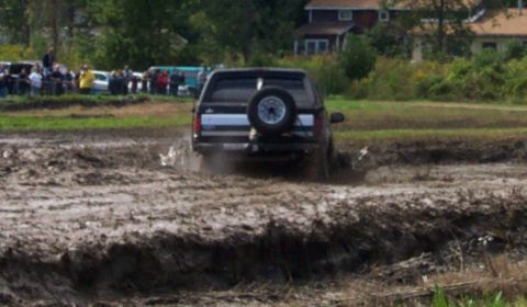 1979 Ford Bronco - A black SUV navigates a muddy track, kicking up water and mud as it goes.