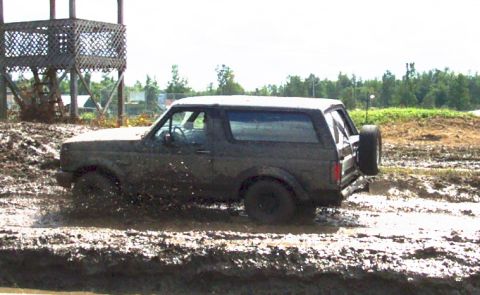 1979 Ford Bronco - This Ford Bronco is navigating a challenging muddy terrain, kicking up water and dirt.