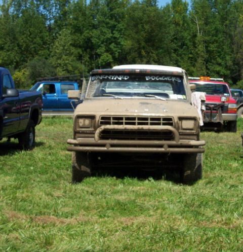 1979 Ford Bronco - A mud-covered pickup truck is parked in a grassy field with other vehicles visible in the background.