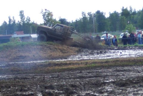 1979 Ford Bronco - A truck navigates a muddy track during a mud bogging event, with spectators watching from the side.