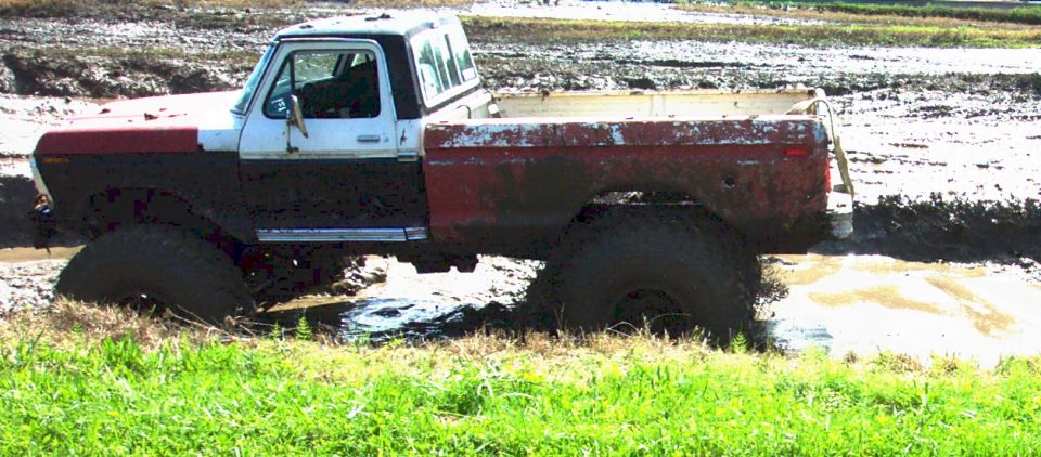 Mud-splattered 1978 Ford Bronco with red and white body stuck in mud, side view