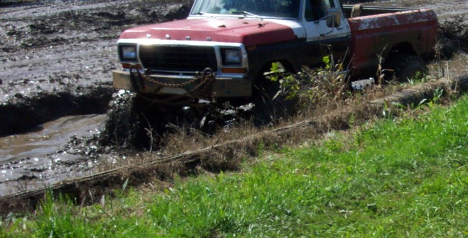 Red and white pickup truck stuck in mud, 3q-front view