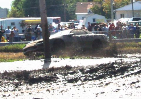 1979 Ford Bronco - A vehicle navigates a muddy track, kicking up dirt as onlookers observe the event.