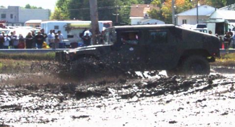 1979 Ford Bronco - A dark SUV navigates a muddy terrain, kicking up dirt and water.