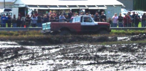 1979 Ford Bronco - A two-tone pickup truck navigates a muddy track with spectators watching.