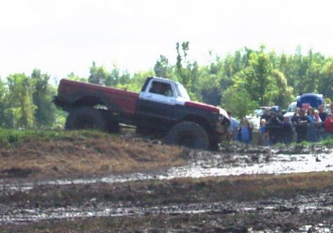 1979 Ford Bronco - A two-tone pickup truck is stuck in a mud pit with spectators observing the scene.