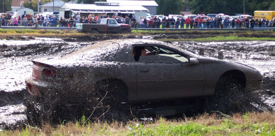 Mud-covered sports car splashing through a mud pit