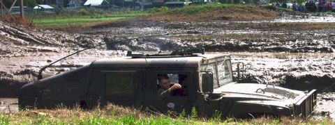 1979 Ford Bronco - A Humvee navigates a muddy obstacle course, with the driver visible through the window.