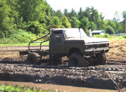 1979 Ford Bronco - This modified truck is deep in the mud, with only its cab and large tires visible.