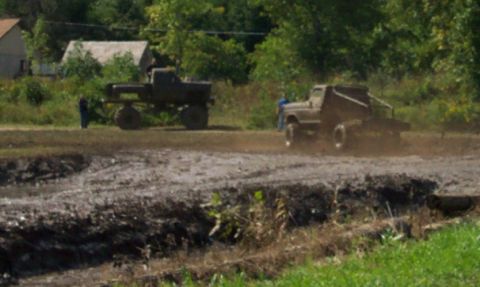 1979 Ford Bronco - Two trucks navigate a muddy track, kicking up dirt and spray.