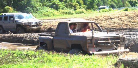 1979 Ford Bronco - Two trucks are stuck in a muddy off-road course during a sunny day.