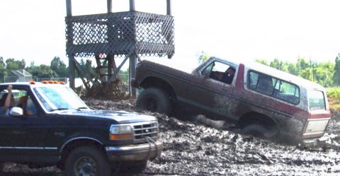 1979 Ford Bronco - Two trucks are stuck in the mud during an off-road event, with a wooden observation deck nearby.