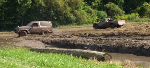 1979 Ford Bronco - Two off-road vehicles navigate a muddy track with trees in the background.