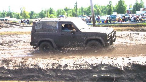 1979 Ford Bronco - A dark SUV navigates a muddy track during an off-road event.