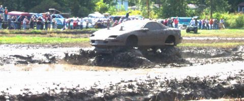 1979 Ford Bronco - A car navigates a mud pit during an event, with spectators watching from the sidelines.