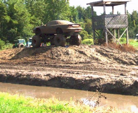 1979 Ford Bronco - A heavily modified car with oversized tires sits atop a muddy hill, with a tractor visible in the distance.