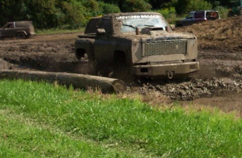 1979 Ford Bronco - A heavily muddied pickup truck navigates a challenging off-road course with other vehicles in the background.