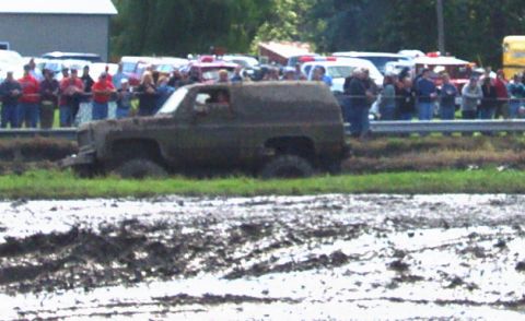 1979 Ford Bronco - A muddy SUV navigates a challenging off-road course with onlookers watching from the sidelines.