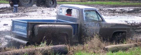 1979 Ford Bronco - A blue Chevrolet pickup truck is stuck deep in the mud, with a person visible through the driver's side window.