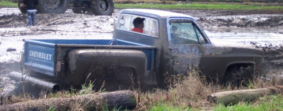 Blue Chevrolet pickup truck stuck in mud with a person inside