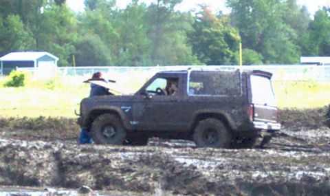 1979 Ford Bronco - A person works on a muddy Ford Bronco that appears to be stuck in a mud pit.