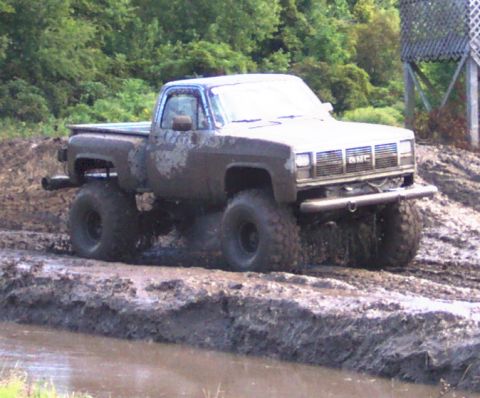 1979 Ford Bronco - A GMC pickup truck navigates a muddy terrain, its tires deep in the muck.