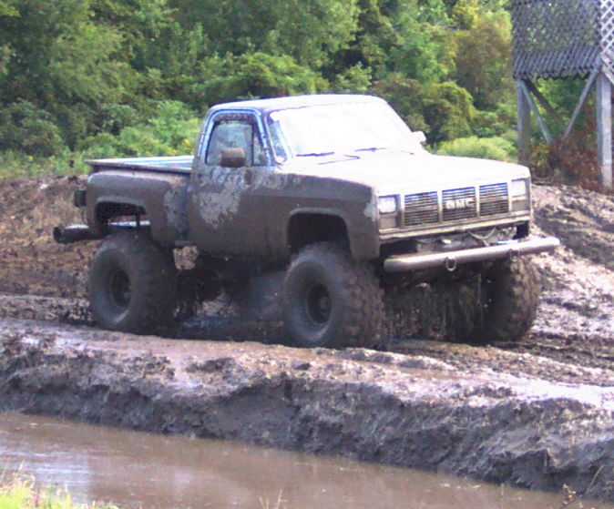 Mud-splattered GMC pickup truck with large tires driving through mud