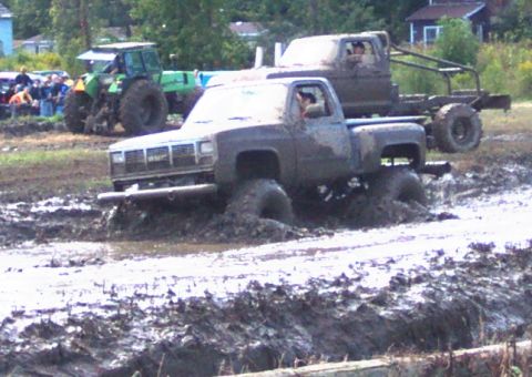 1979 Ford Bronco - Two trucks are stuck in a mud bog, with a tractor and spectators in the background.