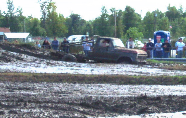 Truck stuck in mud pit with people watching