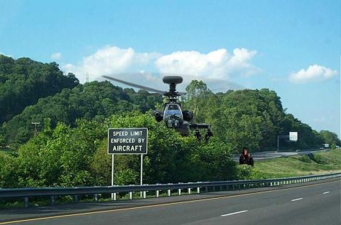 1999 Ford Crown Victoria - An Apache helicopter flies low over a highway, with a sign indicating speed limits are enforced by aircraft.