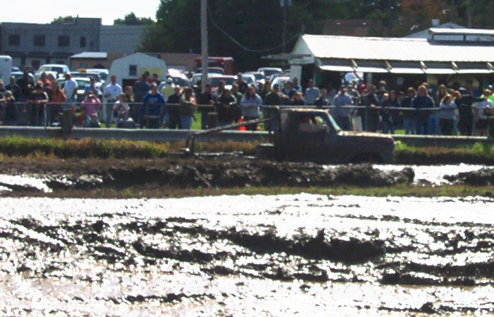 Mud-splattered truck driving through a mud pit with spectators watching