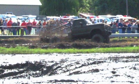 1979 Ford Bronco - A truck navigates a muddy track during a competition, with onlookers watching from the sidelines.