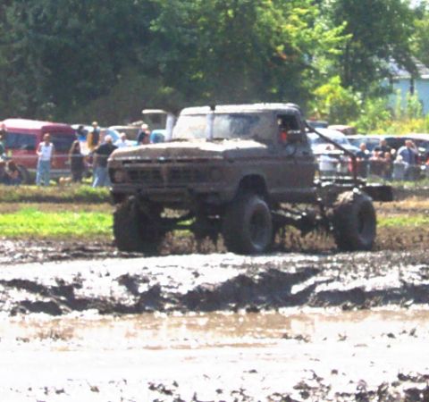 1979 Ford Bronco - Muddy pickup truck navigates a rough terrain, with spectators in the background.