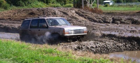 1979 Ford Bronco - A brown Ford Explorer struggles through a muddy obstacle course, kicking up spray.