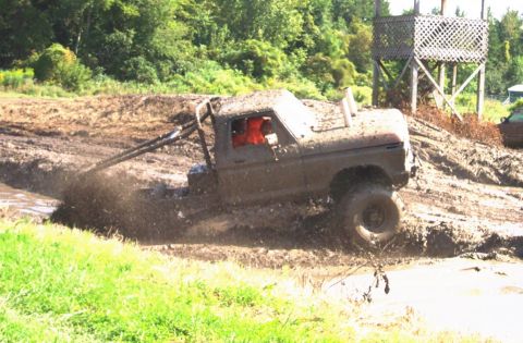 1979 Ford Bronco - 1979 Ford Bronco tackling a mud bog with its modified suspension and roll cage visible.